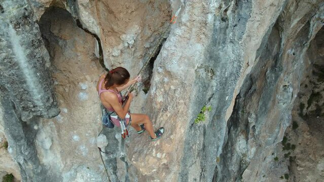 Aerial view of Young fit woman descending on ground after lead rock climbing on sport route on vertical cliff, outdoors rock climbing, cinematic slow motion rock climbing moments
