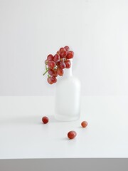 Vertical shot of a bunch of red grape on a glass bottle on white background