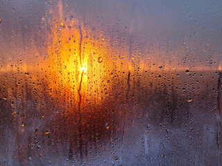 Water drops on a window glass at sunset. Traces of vertically flowing drops and condensate on a...