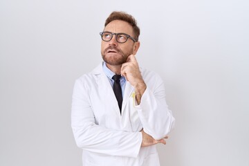 Middle age doctor man with beard wearing white coat with hand on chin thinking about question,...