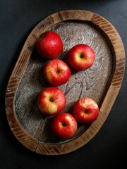 Vertical shot of red apples on a wooden tray on a black table