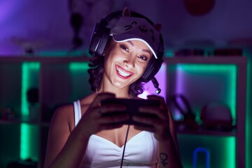 Young beautiful hispanic woman streamer playing video game by smartphone at gaming room