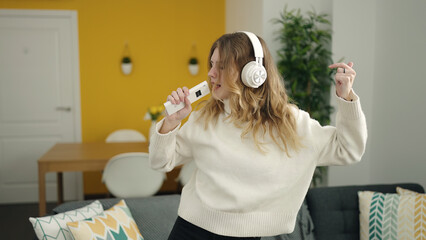 Young blonde woman listening to music and singing song at home