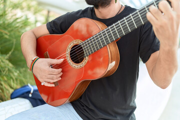 Young hispanic man musician playing classical guitar at park