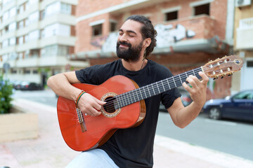 Young hispanic man musician playing classical guitar at street