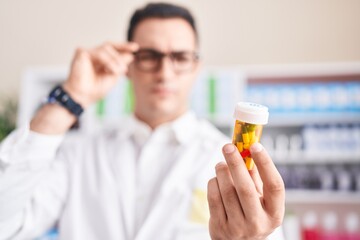 Young hispanic man pharmacist looking pills bottle at pharmacy