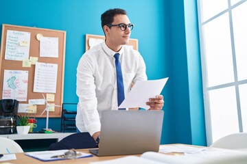 Fototapeta premium Young hispanic man business worker using laptop reading document at office