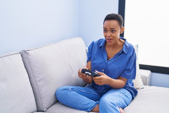 African american woman playing video game sitting on sofa at home