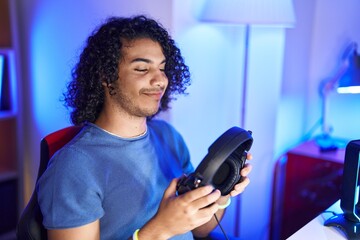 Fototapeta na wymiar Young latin man streamer smiling confident holding headphones at gaming room