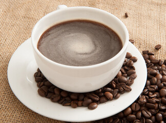 Cup of coffee on a saucer with coffee beans on a background of burlap