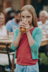 Little girl enjoying fresh juice while spending time with her family outdoors