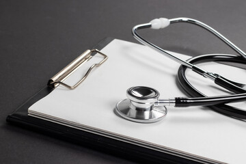 A clipboard and stethoscope with white paper on it, set against a dark background