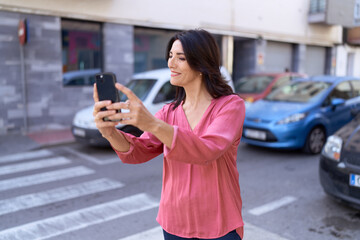 Middle age hispanic woman smiling confident making selfie by the smartphone at street