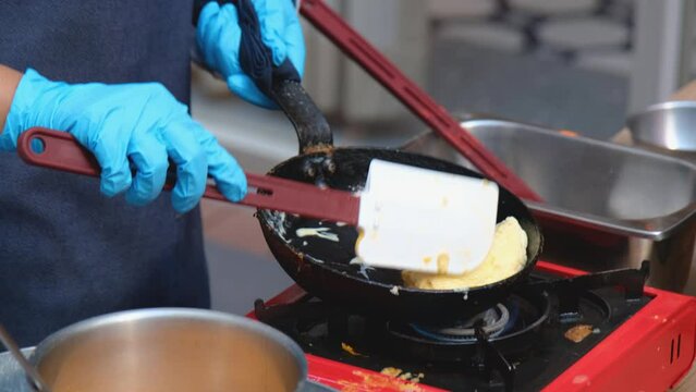 A cook is using a plastic spatula to make an omelet in a pan.