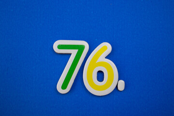 Placed on a blue background, photographed from above, the number 76.