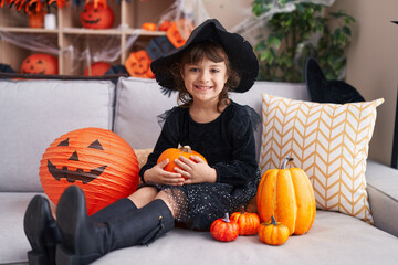 Adorable hispanic girl having halloween party holding pumpkin at home