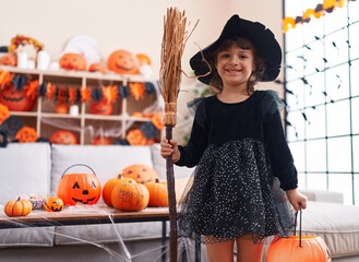 Adorable hispanic girl having halloween party holding broom at home