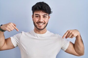 Hispanic man with beard standing over white background looking confident with smile on face,...
