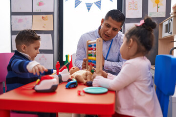 Hispanic man with boy and girl playing with abacus sitting on table at kindergarten