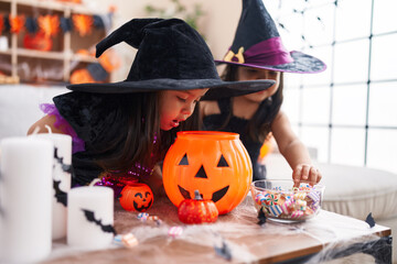 Adorable twin girls having halloween party holding candies at home