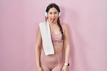 Young brunette woman wearing sportswear and headphones sticking tongue out happy with funny...