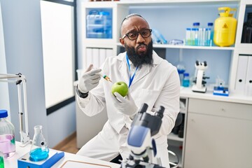 African american man working at scientist laboratory with apple looking at the camera blowing a kiss being lovely and sexy. love expression.
