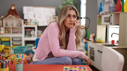 Young blonde woman teacher sitting on table stressed at kindergarten