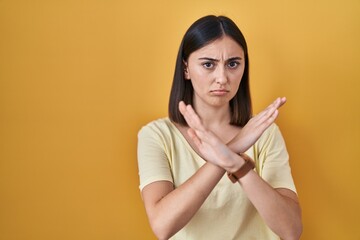 Obraz premium Hispanic girl wearing casual t shirt over yellow background rejection expression crossing arms doing negative sign, angry face
