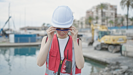 Obraz premium Young beautiful hispanic woman builder standing with serious expression wearing glasses at seaside