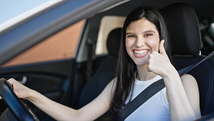 Fototapeta na wymiar Young beautiful hispanic woman sitting on car doing thumb up gesture at street