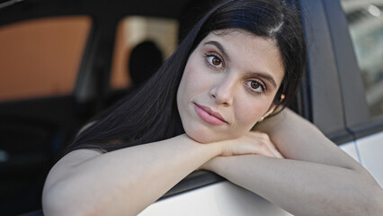 Fototapeta na wymiar Young beautiful hispanic woman sitting on car with relaxed expressi at street