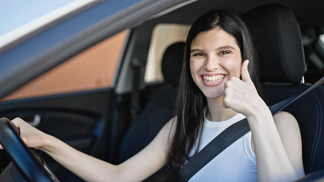 Young beautiful hispanic woman sitting on car doing thumb up gesture at street