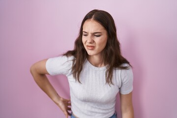 Young hispanic girl standing over pink background suffering of backache, touching back with hand, muscular pain