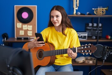 Fototapeta na wymiar Young woman musician playing classical guitar using smartphone at music studio