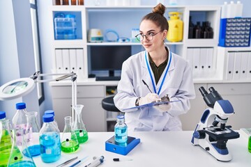 Young woman scientist measuring liquid writing on document at laboratory