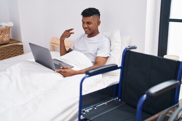 Young hispanic man lying on the bed, using wheelchair smiling happy pointing with hand and finger