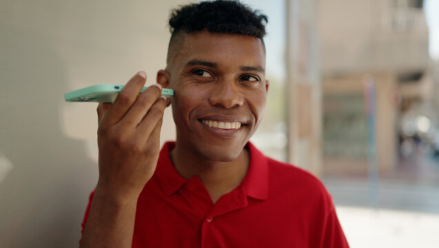 Young latin man smiling confident listening audio message by the smartphone at street
