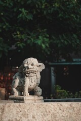 Vertical shot of a Chinese lion sculpture in the park with trees in the background