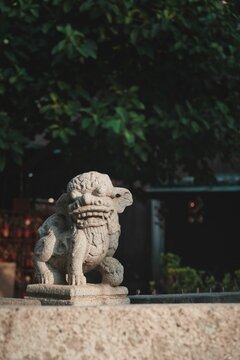 Vertical shot of a Chinese lion sculpture in the park with trees in the background © Hys/Wirestock Creators