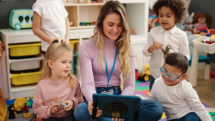 Woman and group of kids having lesson using touchpad at kindergarten