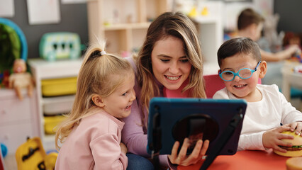 Woman and group of kids having lesson using touchpad at kindergarten