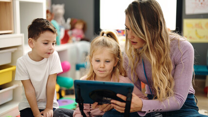 Woman with boy and girl having lesson using touchpad at kindergarten