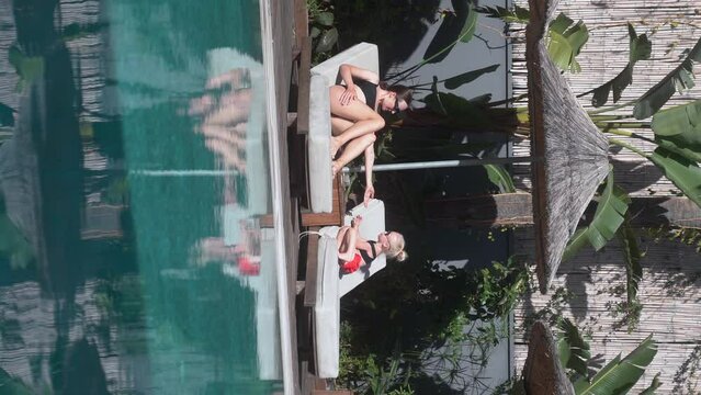 A young mother and her young daughter sunbathe together and spend time by the pool