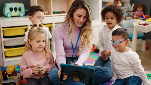 Woman and group of kids having lesson using touchpad at kindergarten