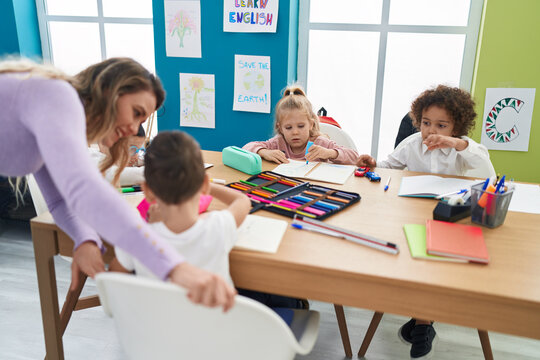 Woman and group of kids having lesson sitting on table at classroom