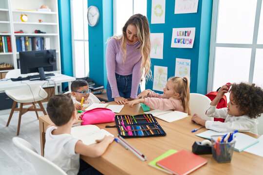 Woman and group of kids having lesson sitting on table at classroom