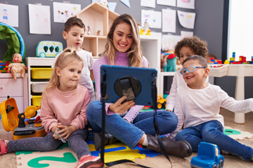 Woman and group of kids having lesson using touchpad at kindergarten