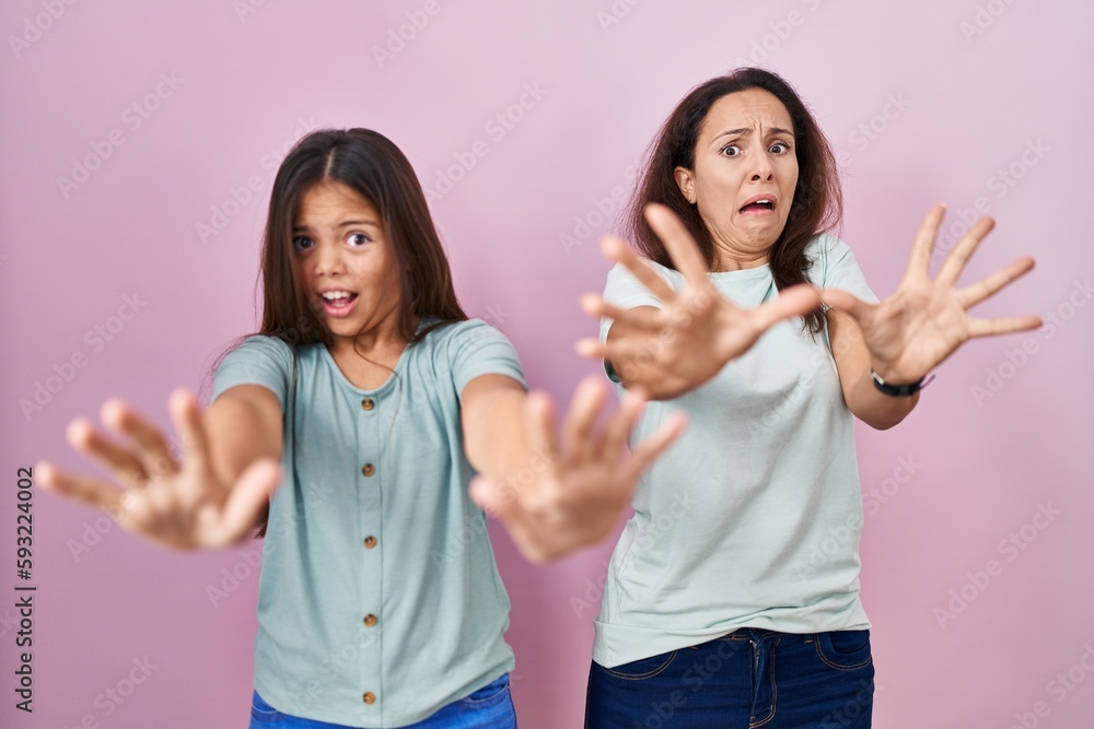 Poster Young mother and daughter standing over pink background afraid and terrified with fear expression stop gesture with hands, shouting in shock. panic concept.