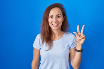 Fototapeta premium Brunette woman standing over blue background showing and pointing up with fingers number three while smiling confident and happy.