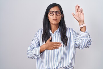 Young hispanic woman wearing glasses swearing with hand on chest and open palm, making a loyalty...